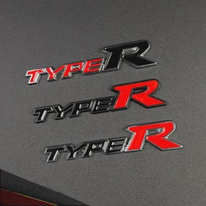 May include: Three metallic "TYPE R" emblems. The "TYPE" text is silver with red accents, and the "R" is red with a black outline. The emblems are on a dark gray textured surface.