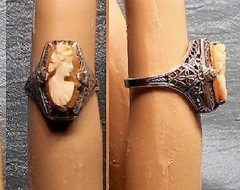 May include: A silver filigree ring with a cameo featuring a woman's profile. The cameo is made of a light brown material and is set in a silver ring.