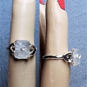 May include: A silver ring with a clear, square-shaped stone set in a floral design. The stone has a small, clear diamond in the center.