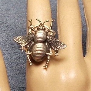 Può includere: Un anello color oro con un designo di ape dettagliato con ali e gambe intricate.