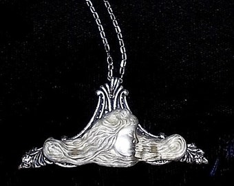 May include: A silver necklace with a pendant featuring a woman's face with flowing hair. The pendant is detailed and intricate.