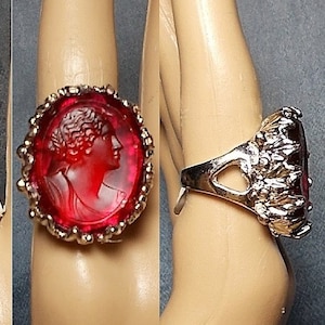 May include: A gold ring with a red cameo featuring a woman's profile. The ring has a decorative design around the cameo.