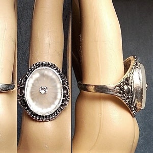 May include: A silver ring with a white oval stone set in a black bezel. The stone has a small clear crystal in the center.