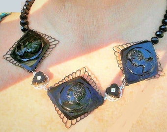 May include: A black glass necklace with three square pendants featuring cameo-like images of women's profiles. The necklace is made with black beads and silver-toned metal accents.