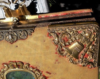 May include: An antique photo album with a worn leather cover and ornate brass accents. The album has a decorative brass clasp and a small bell-shaped design on the front cover.