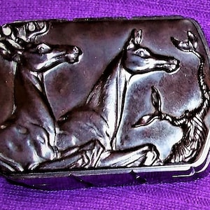 May include: A vintage black and brown compact with a detailed design of two horses. The compact is rectangular in shape and has a textured surface.