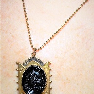 May include: A gold chain necklace with a black cameo pendant. The pendant is set in a gold frame with intricate details. The cameo features a woman's profile.