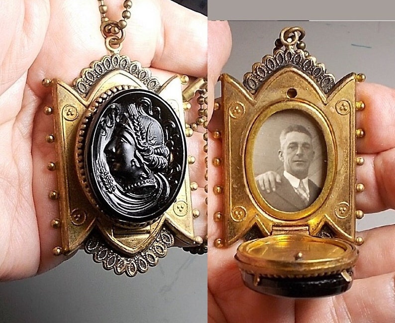 May include: A gold locket necklace with a black cameo and a photo of a man inside. The locket has a decorative design and is open to reveal the photo.
