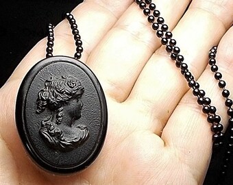 May include: A black cameo necklace with a black oval pendant featuring a woman's profile in relief. The necklace is made of black beads.