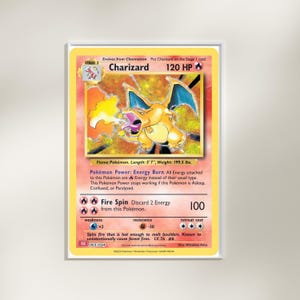Può includere: Una carta Pokémon Charizard incorniciata. La carta presenta un drago arancione con ali blu, chiamato "Charizard" con 120 HP. Il testo include "Fire Spin" e altri dettagli del gioco. La carta è lunga 1,70 m e pesa 90,5 kg.