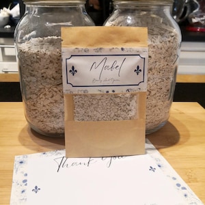 May include: Two glass jars with metal lids filled with oats, a small paper bag labelled "Mabel", and a card that says "Thank you". The bag has a clear window showing the oats inside. The card has a floral design.