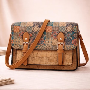 May include: A rectangular crossbody bag with a cork body and a flap featuring a colorful geometric pattern. The bag has a brown shoulder strap and two buckle closures. The bag is approximately 10 inches wide.