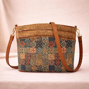 Könnte beinhalten: Eine Umhängetasche mit einem Oberteil aus Kork und einer gemusterten Vorderseite. Die Vorderseite hat ein Patchwork-Design mit blauen, roten und beigen geometrischen Formen. Die Tasche hat einen braunen Riemen und goldfarbene Beschläge.