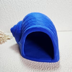 May include: A vibrant blue, seashell-shaped decorative item. The shell has a textured surface with a geometric pattern and a large opening. The item is designed to resemble a natural seashell, perfect for home decor.
