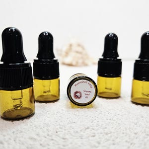 May include: Five small amber glass bottles with black droppers. One bottle has a label that reads "Moonshell Keep Sesame Seed Oil". The bottles are arranged on a white surface.