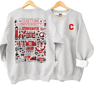 May include: Two light gray sweatshirts hanging on wooden hangers. One sweatshirt features a large graphic with the text "CUSTOM UNIVERSITY" and various illustrations in red and black. The other sweatshirt has a large red "C" on the chest.