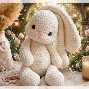 May include: A handmade, off-white crochet bunny with long, floppy ears and pink cheeks. The plush toy is sitting on a table with a lit candle, a vase of dried flowers, and a small bag with the name "Elya" embroidered on it. The background features a garden setting with roses.