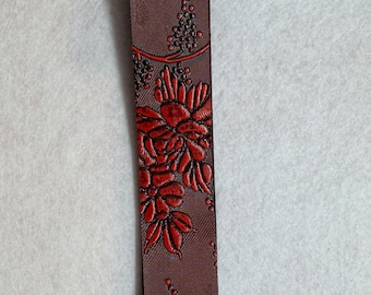 May include: A burgundy wristlet key fob with a floral and grape design in red. The key fob has a black metal loop and ring for attaching keys. The floral pattern is embossed on the fabric.