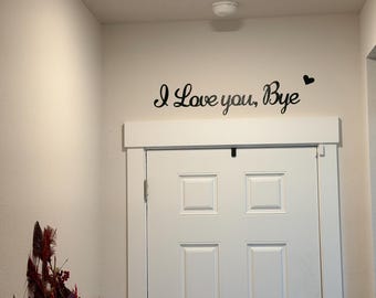 May include: A white door with a decorative trim and the words "I Love you, Bye" in black script on the wall above it. A small black heart is next to the word "Bye".