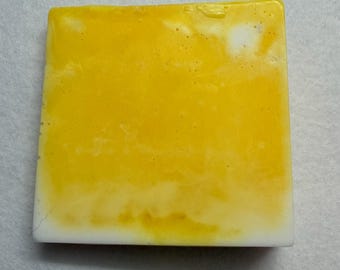May include: A square bar of soap with a yellow and white marbled design. The soap has a smooth, glossy surface and a rectangular shape. The colors blend together, creating a unique pattern. The soap is likely handmade.