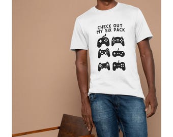 May include: White t-shirt with the text "CHECK OUT MY SIX PACK" above six black controller graphics. The person in the image is wearing blue jeans and is smiling.