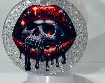 May include: A round keychain with a glittery silver border. The design features a pair of red lips with a skull inside, and black liquid dripping down. The keychain is attached to a silver chain.