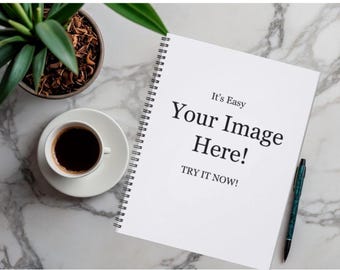 May include: A white spiral-bound notebook with black text that reads It's Easy Your Image Here! TRY IT NOW! positioned next to a cup of black coffee on a saucer, a green potted plant, and a dark green pen on a white marble surface.