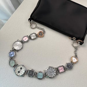 May include: A black rectangular handbag featuring a unique shoulder strap constructed from a series of various analogue wristwatches linked together. The watches vary in shape, size, and dial colour, including silver, pink, blue, and black faces.