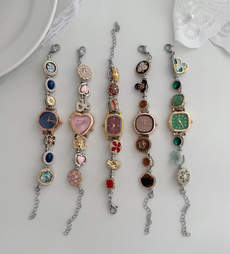 K&ouml;nnte beinhalten: F&uuml;nf dekorative Armbanduhren mit verschiedenfarbigen Zifferbl&auml;ttern und dekorativen Anh&auml;ngern. Die Zifferbl&auml;tter sind in Blau-, Rosa- und Gr&uuml;nt&ouml;nen gehalten. Zu den Anh&auml;ngern geh&ouml;ren Herzen, Blumen und Edelsteine. Die Uhren haben silberfarbene Kettenarmb&auml;nder.