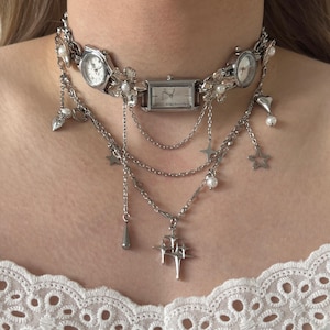 Puede incluir: Collar gargantilla plateado con múltiples esferas de reloj, detalles florales y colgantes. El collar incluye una esfera rectangular y varias esferas redondas. Los colgantes incluyen estrellas, lágrimas y perlas. El collar se lleva alrededor del cuello.