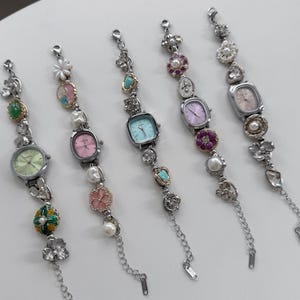 May include: Five silver-toned bracelet watches with various pastel-colored watch faces. Each watch features decorative elements like pearls, flowers, and gemstones. The watch faces are in shades of pink, green, and blue.