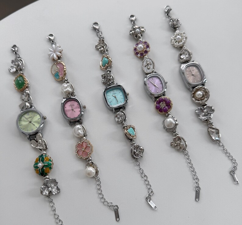 May include: Five silver-toned bracelet watches with various pastel-colored watch faces. Each watch features decorative elements like pearls, flowers, and gemstones. The watch faces are in shades of pink, green, and blue.