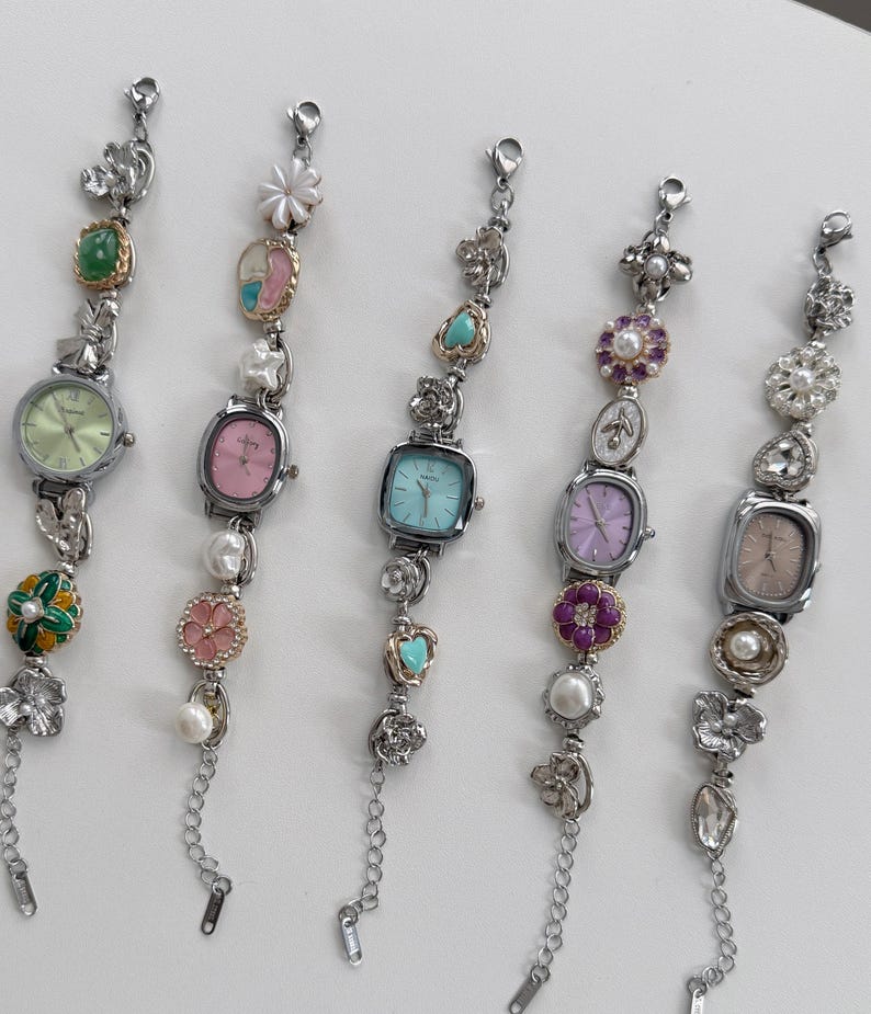 May include: Five silver-toned wristwatches with decorative embellishments. Each watch features a different colored face, including green, pink, and blue. The bands are adorned with pearls, flowers, and other decorative elements.