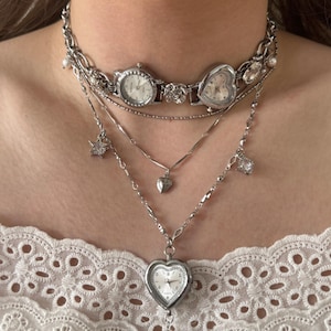 May include: A multi-layered silver necklace with watch faces, charms, and a heart-shaped pendant. The necklace includes a choker with two watch faces and a heart-shaped watch. Additional layers have star, heart, and crystal charms.