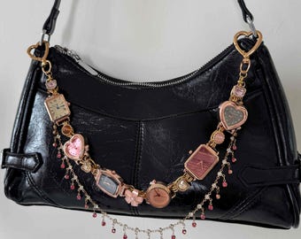 May include: Black leather shoulder bag adorned with a chain of vintage watches. The chain includes square and heart-shaped watches, with pink and gold detailing. Small pink beads hang from the chain, adding a touch of elegance.