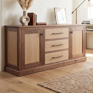 May include: A rectangular wooden sideboard featuring a dark walnut frame with lighter oak-toned panels on the two side doors and three central drawers. Each drawer and door is fitted with a slim, dark metal handle for a clean, functional design.