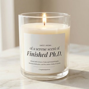 May include: A clear glass candle with a white wax fill and a lit wick. The label features black text reading: SWEET AROMA of a serene scent of Finished Ph.D. Infused with echoes of late-night breakthroughs, relentless dedication, and the serene clarity of success. Congratulations.
