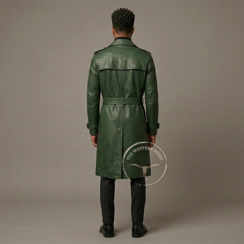 May include: A long, green leather trench coat with a belt, worn by a person. The coat has a classic design with a collar and button details. The person is wearing black pants and shoes. The Western Hides logo is visible.