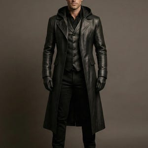 Puede incluir: Un abrigo largo de cuero negro con capucha, usado sobre un chaleco y camisa negros. El abrigo llega hasta los tobillos y tiene un corte entallado. El conjunto incluye guantes y pantalones negros, creando un conjunto monocromático.