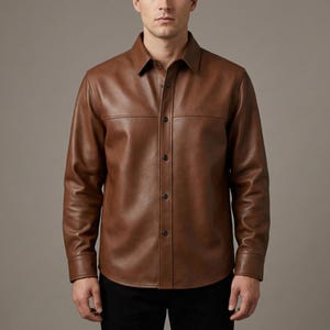 May include: A brown leather shirt with a button-down front and a collared neckline. The shirt has long sleeves and is made of a smooth, supple leather. The shirt is worn with black trousers.