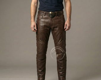 May include: Brown leather pants with decorative stitching and padded knee details. The pants feature a skull-shaped belt buckle. The overall style suggests a biker or motorcycle theme.