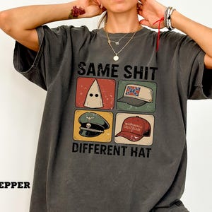 Pode incluir: T-shirt cinza escuro com o texto "SAME SHIT DIFFERENT HAT" e quatro ilustrações. A camisa tem um visual vintage. A palavra "PEPPER" está impressa no canto inferior esquerdo.