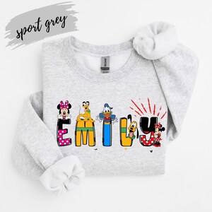 Op de afbeelding: Een lichtgrijs sweatshirt met de naam "EMILY" in kleurrijke letters met Disney-thema. Minnie Mouse, Donald Duck en Pluto zijn afgebeeld. De woorden "sport grey" staan in cursiefschrift linksboven.
