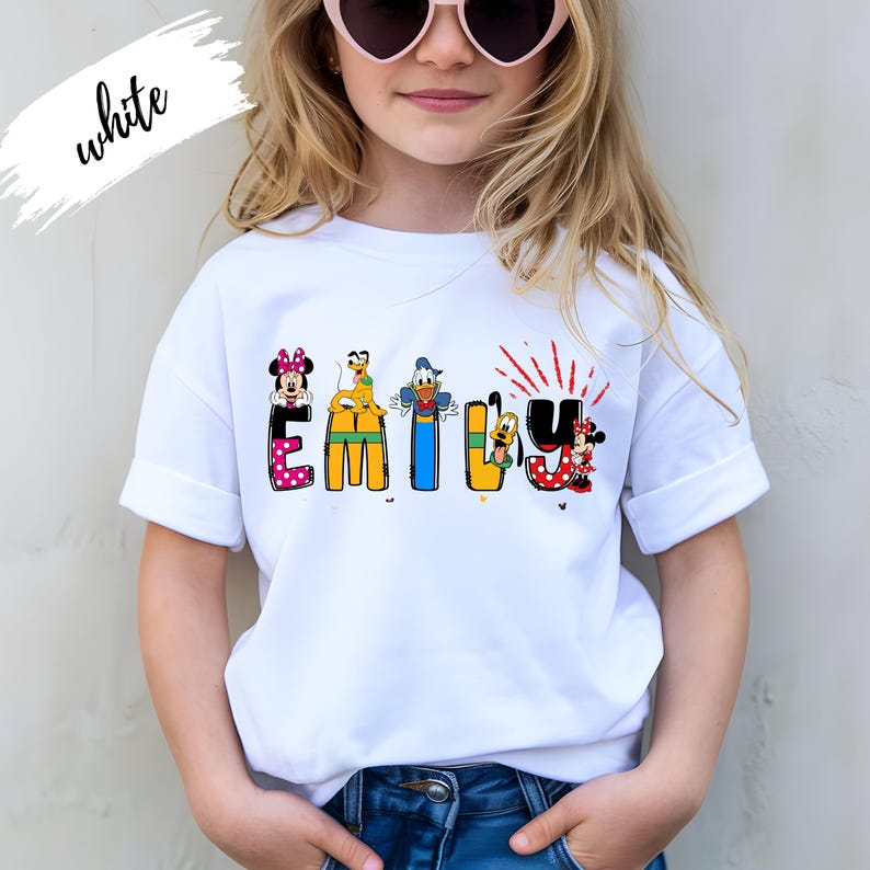 Op de afbeelding: Wit T-shirt met de naam "Emily" in kleurrijke, cartoonachtige letters. Elke letter is versierd met Disney-figuren, waaronder Minnie Mouse, Donald Duck en Pluto. Het woord "white" staat in cursiefschrift linksboven.