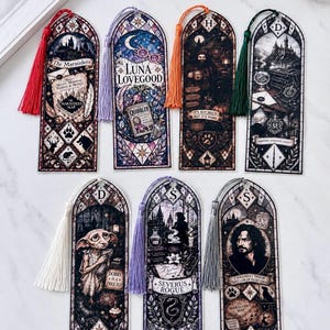 Pode incluir: Sete marcadores de página retangulares com ilustrações em estilo vitral de personagens e símbolos da série Harry Potter. Cada marcador inclui uma borla colorida no topo e arte detalhada com etiquetas de texto para cada personagem.