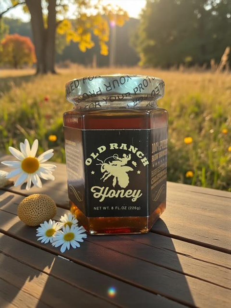 Puede incluir: Un tarro de miel Old Ranch, con una etiqueta que presenta una ilustraci&oacute;n de abeja, se encuentra sobre una superficie de madera. El tarro contiene miel de color &aacute;mbar y est&aacute; rodeado de margaritas y un peque&ntilde;o objeto texturizado. La etiqueta dice "Peso neto 226g".
