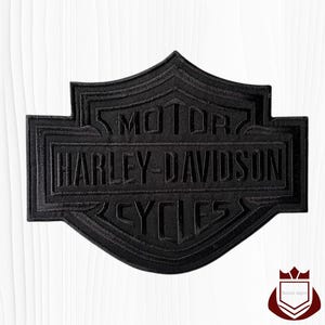 May include: Black Harley-Davidson patch with raised lettering. The patch features the Harley-Davidson logo, including the words "MOTOR HARLEY-DAVIDSON CYCLES" in a shield shape. The patch is likely for a jacket or vest.