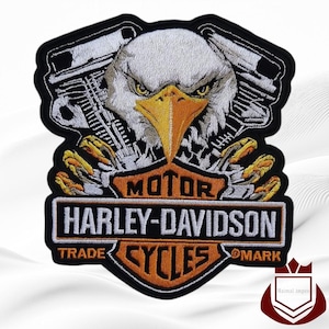 May include: Embroidered patch featuring a detailed eagle head with a yellow beak and piercing eyes, set against a motorcycle engine design. The patch includes the text "MOTOR HARLEY-DAVIDSON CYCLES TRADE MARK" in orange and white.