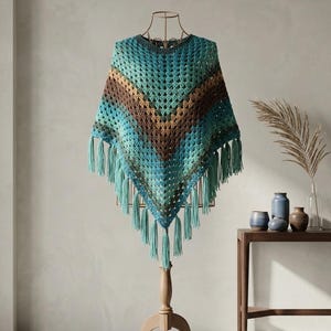 Puede incluir: Un poncho de ganchillo con un patrón en forma de V y rayas horizontales en tonos azul verdoso, turquesa, marrón y verde oscuro. La prenda tiene un diseño de punto abierto texturizado y está rematada con largos flecos colgantes en el borde.