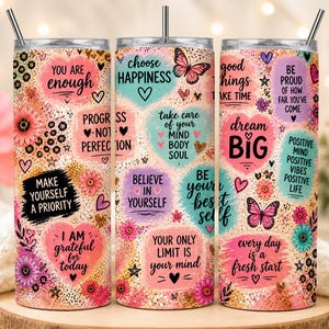 May include: Three stainless steel tumblers with lids and straws, decorated with floral patterns and inspirational quotes. The tumblers feature phrases like "You are enough" and "Dream Big" in various colors.